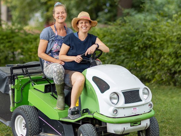 Zwei Gärtnerinnen sitzen auf einem grossen Motor-Rasenmäher.
