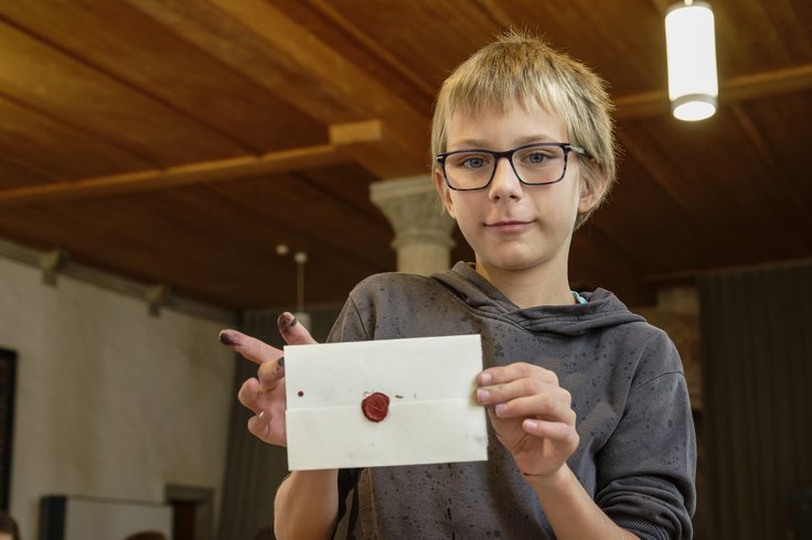Ein Bub zeigt einen Brief mit Siegel aus Wachs (Workshop für Schulen Klosterhalbinsel Wettingen)