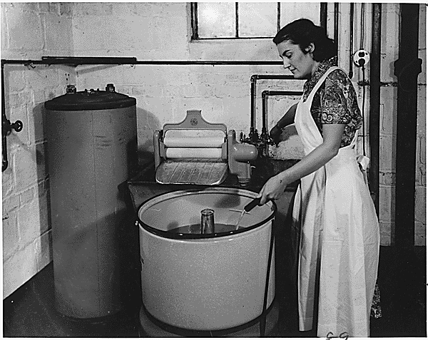 Bild (schwarz und Weiss): Eine Frau steht vor einer Waschmaschine.