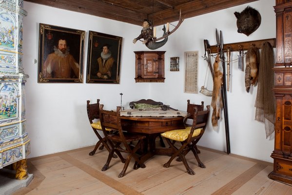 Eine Fotografie der rekonstruierten Landvogtstube im Wohnmuseum des Schloss Lenzburg. Zu sehen ist ein Holztisch mit Stühlen, zwei Gemälde an der Wand, diverse Jagdutensilien sowie Jagdtrophäen.