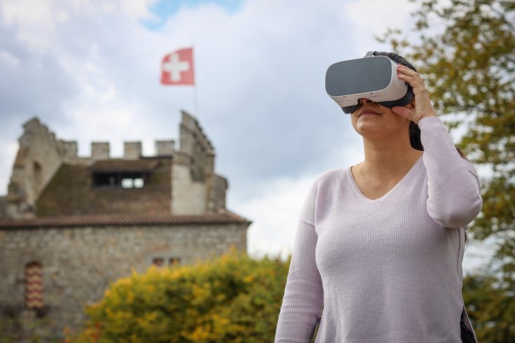 Besucherin vor dem Schloss Habsburg mit der schweizer Fahne mit der VR-Brille