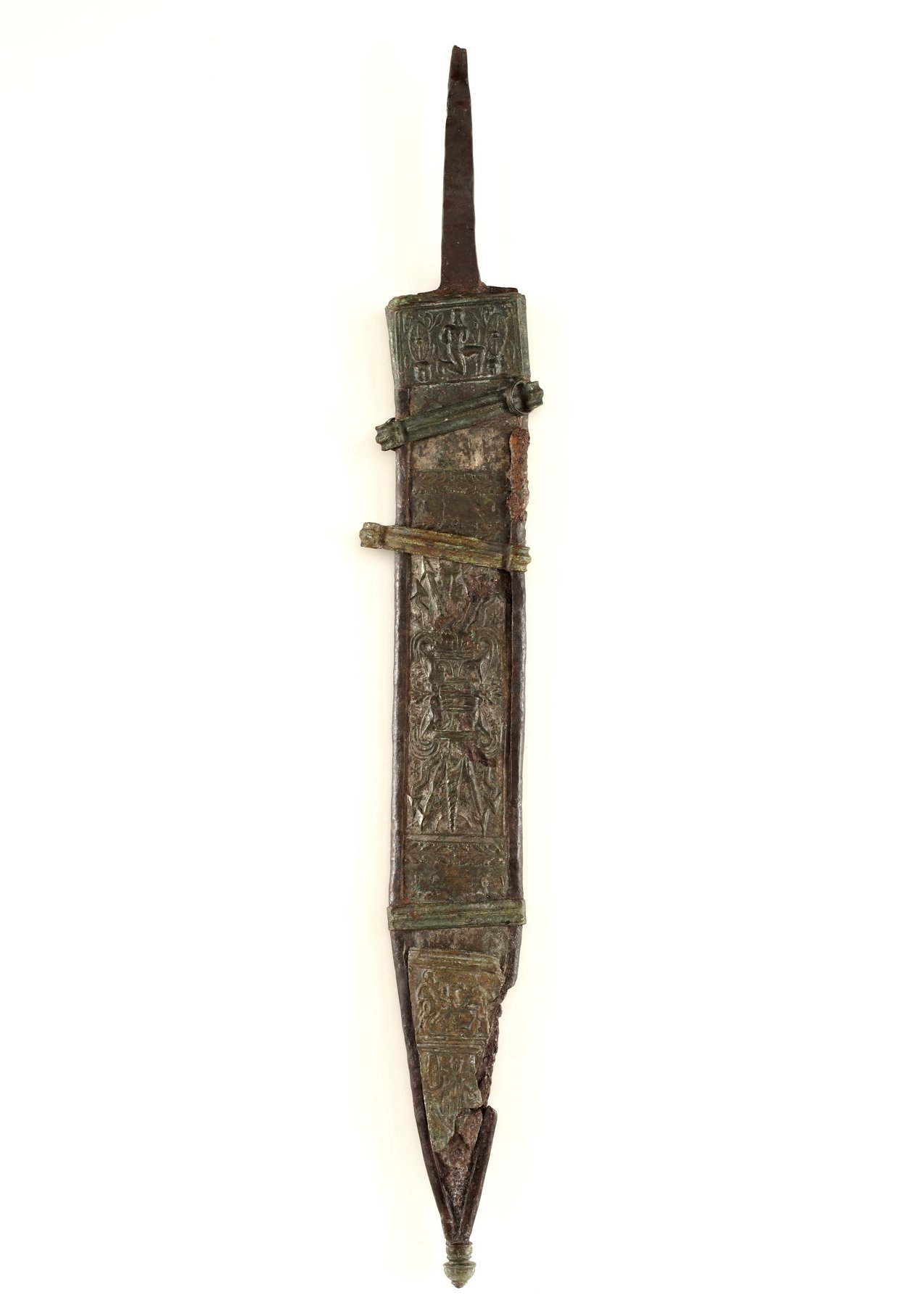 Vor einem weissen Hintergrund ist die Schwertscheide eines Kurzschwertes zu sehen. Diese Schwertscheide ist aus Bronzeblech gefertigt und mit kunstvollen Verzierungen verziert. 