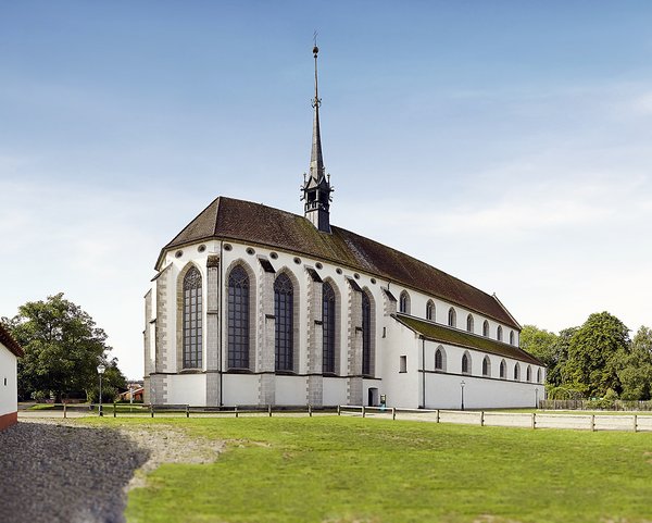 Das Bild zeigt eine Aussenaufnahme der ehemaligen Klosterkirche des Klosters Königsfelden. Die Kirche ist von einer grünen Wiese und einem blauen Himmel umgeben. 