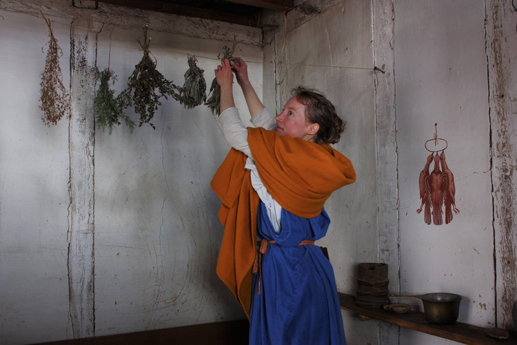 Aufnahme einer Person in römischer Kleidung. Sie hängt diverse Kräuter zum Trocknen auf, darunter auch Salbei.