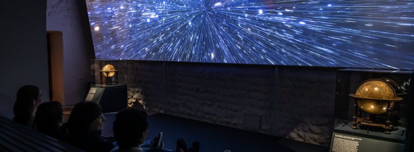 Ausstellung "Observatorium" auf der Klosterhalbinsel Wettingen: Grosse Leinwand mit Sternenhimmel, davor Schülerinnen und Schüler im dunklen Zuschauerraum.