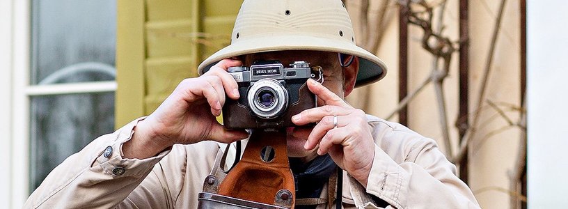 Ein Mann im Expeditionsoutfit mit Kamera vor dem Gesicht. Er fotografiert.