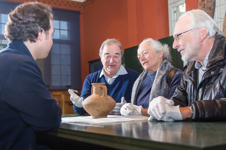 Vier Männer sitzen an einem Tisch vor einem alten Originalobjekt und diskutieren.