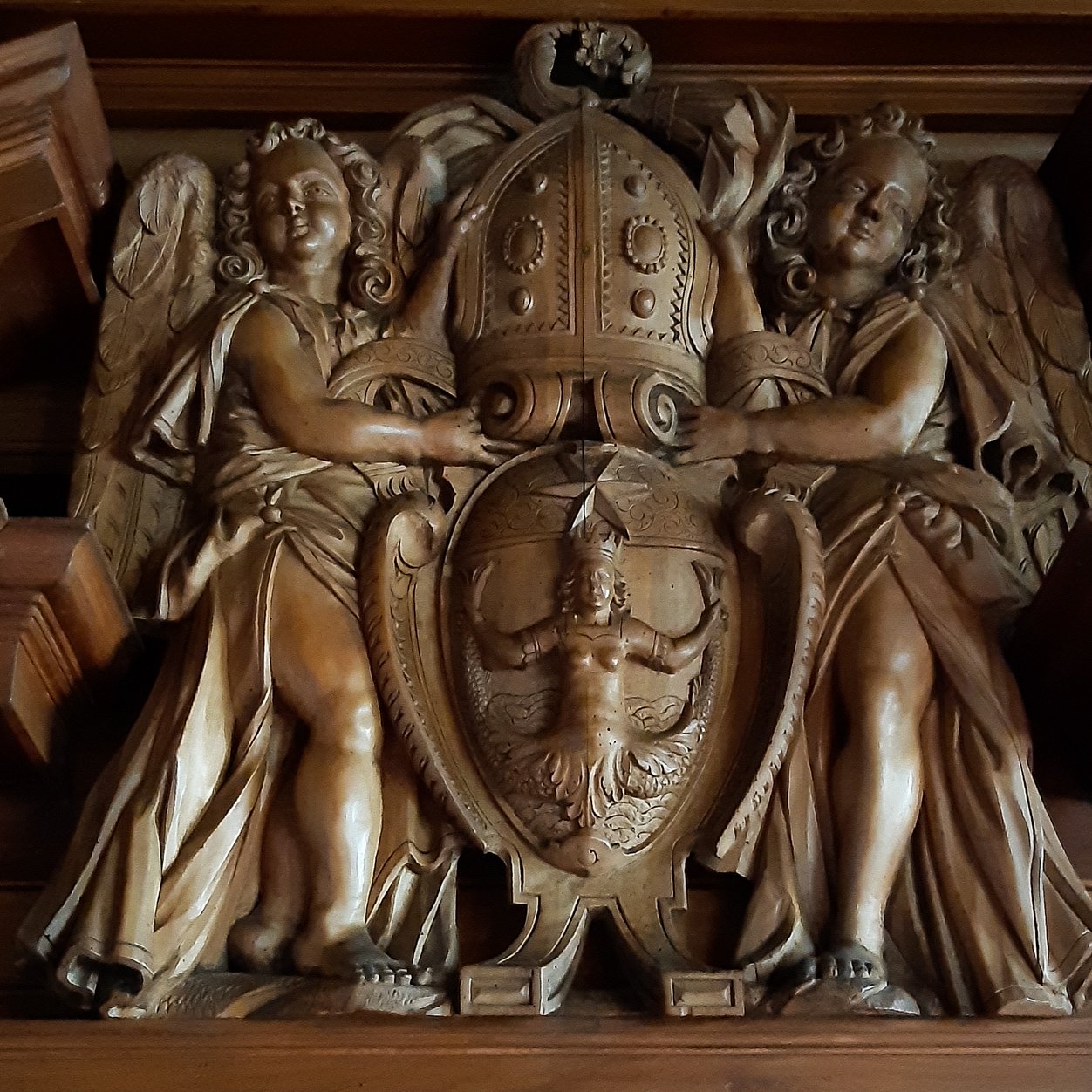 Darstellung einer Meerjungfrau mit zwei Schwanzflossen. Zwei Engel tragen die Wappen. 