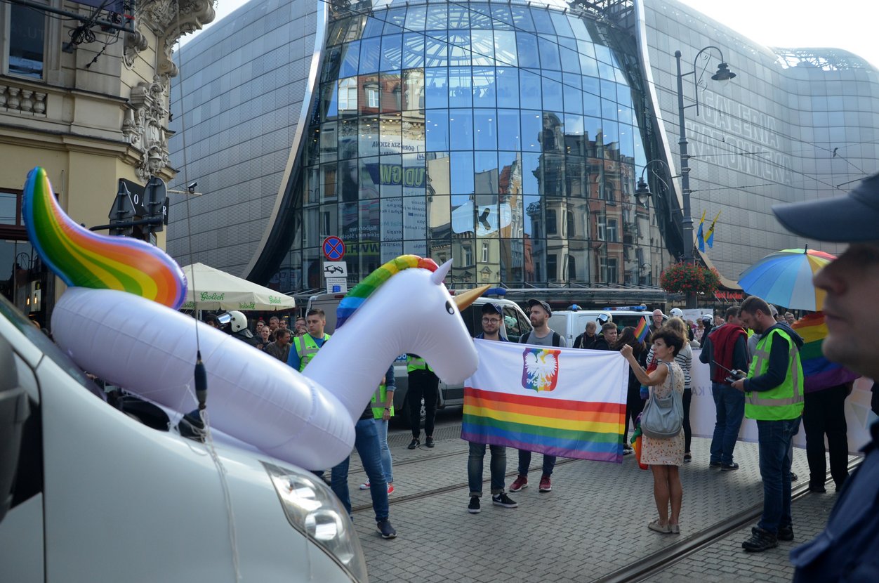 Pride: Menschenmenge, die unter anderem einen Schwingring in Form eines Einhorns mit regenbogenfarbigen Schweif und Mähne sowie der Pride-Fahne tragen.