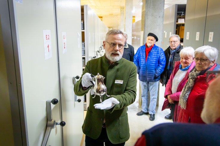 Ein Mann präsentiert im Sammlungszentrum Egliswil einen historischen Kelch. Neben und hinter dem Mann steht eine Besuchergruppe.