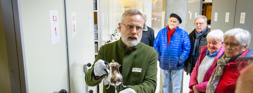 Ein Mann präsentiert im Sammlungszentrum Egliswil einen historischen Kelch. Neben und hinter dem Mann steht eine Besuchergruppe.