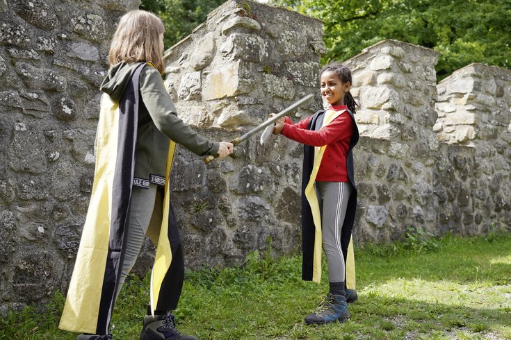 Zwei Schülerinnen im Schwertkampf vor den Zinnen im Workshop für Schulen Schloss Hallwyl