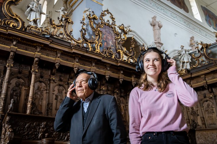 Ein Mann und eine Frau stehen in der Mönchskirche der Klosterhalbinsel Wettingen. Sie tragen grosse Kopfhörer. Das Mädchen lacht.