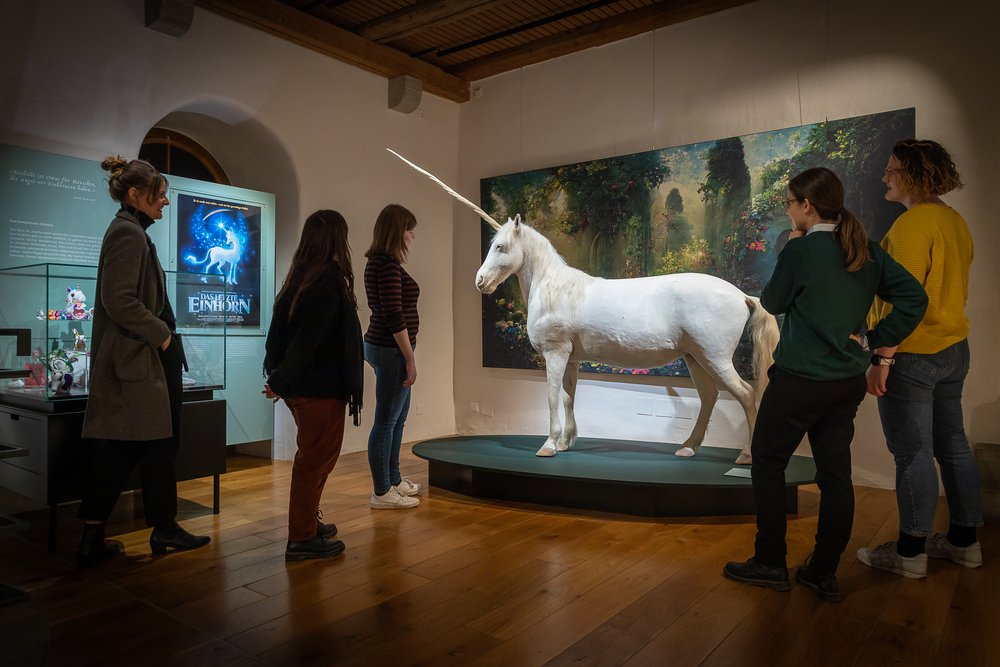 Blick in die Ausstellung "Einhorn - eine fabelhafte Geschichte" auf Schloss Lenzburg. Ein lebensgrosses Einhorn, darum herum Besucherinnen und Besucher.