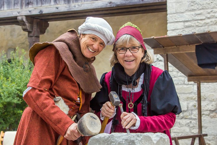 Zwei mittelalterlich gekleidete Frauen bearbeiten einen Stein.