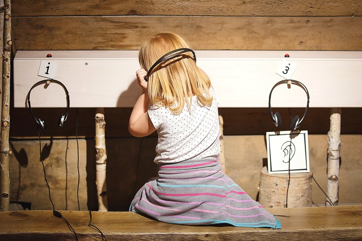 Mädchen hört mit dem Rücken gewandt und Kopfhörern in der Kinderstube gespannt zu auf Schloss Wildegg