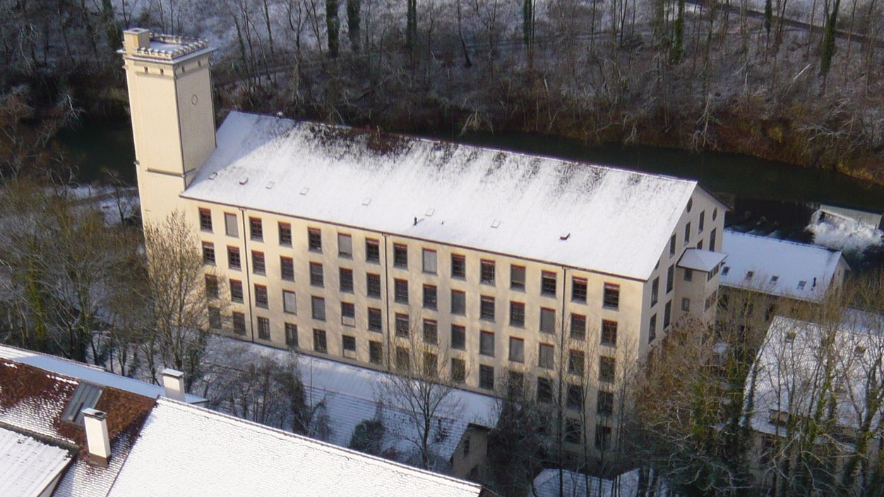 Luftaufnahme des Hauptgebäudes der Spinnerei Wettingen, auf dem Dach liegt Schnee.