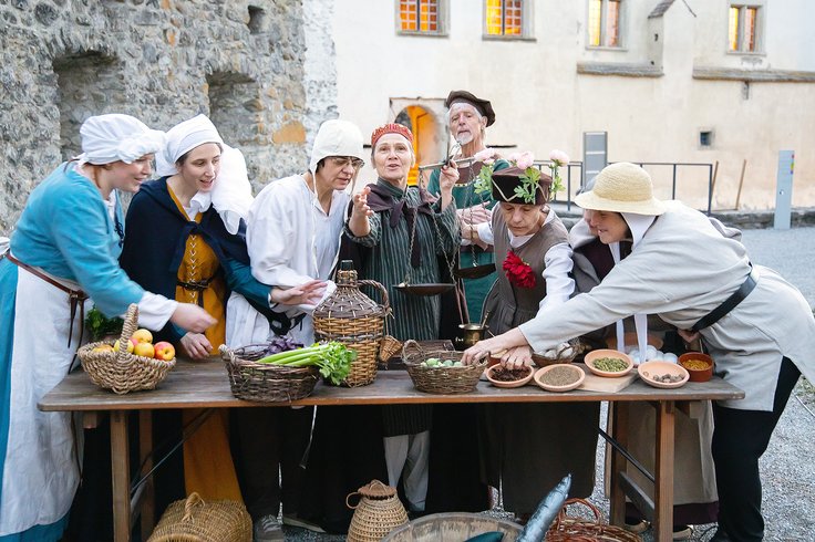 Eine Gruppe Schauspielerinnen und Schauspieler, vor ihnen ein gedeckter Markt-Stand