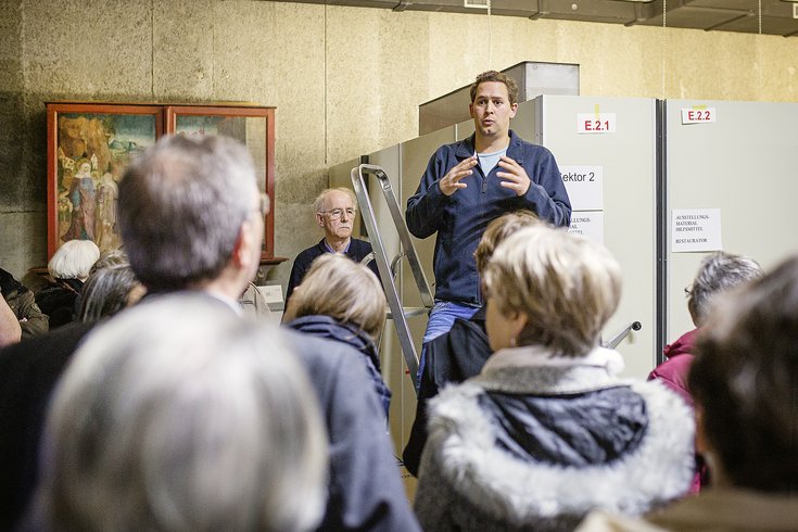 Ein Mitarbeiter steht auf einer Leiter und spricht zur Besuchergruppe