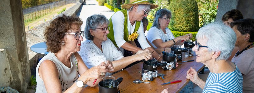 Workshop im Garten: Eine Gruppe Frauen setzt am Tisch und kocht Salbe; im Hintergrund der Garten von Schloss Wildegg
