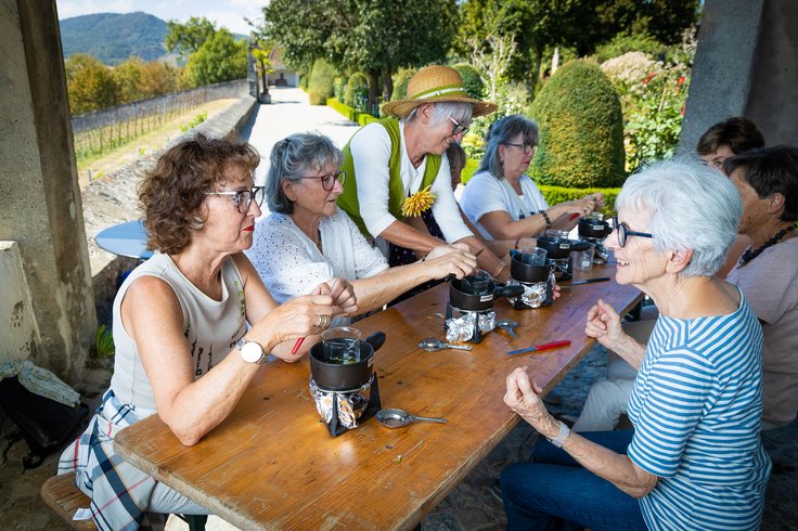 Workshop im Garten: Eine Gruppe Frauen setzt am Tisch und kocht Salbe; im Hintergrund der Garten von Schloss Wildegg