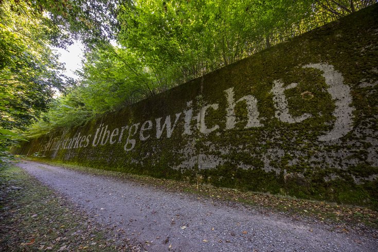 Kulturweg Limmat: Ein Weg mit einer langen Steinwand, auf der Wörter geschrieben sind.