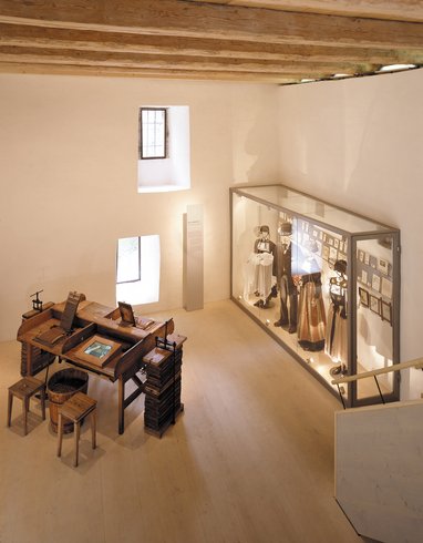 Blick zu einem ausgestellten, antiken Tisch und historische Kleider im Ausstellungsraum im Kornhaus Schloss Hallwyl