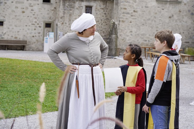 Die Magd im Workshop "Besuch im Schloss Hallwyl" redet mit zwei Kindern