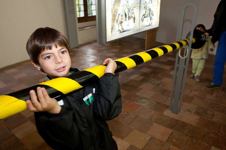 Junge greift nach einer ausgestellten schwarz-gelb gestreiften Lanze in der Dauerausstellung im Schloss Hallwyl