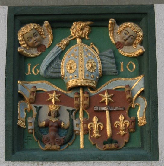 Abbildung des Wappens des Klosters. In den oberen Ecken zwei vergoldete Engelsköpfe. Unten links eine Meerjungfrau.