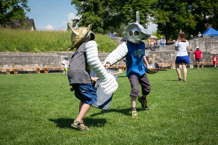 Zwei Kinder mit Helm kämpfen gegeneinander wie Gladiatoren.