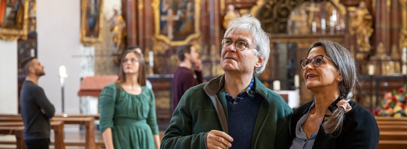 Ein Ehepaar steht in der Klosterkirche Wettingen und blickt staunend in die Höhe. Dahinter weitere Personen in Unschärfe.