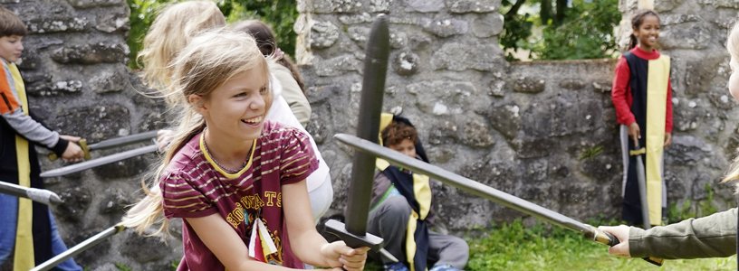 Workshop "Feste Burg Schloss Hallwyl" Kinder haben zusammen spass im Schwertkampf mit Zinnen im Hintergrund