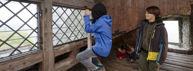 Zwei Schüler unter dem Dach von Schloss Habsburg; ein Bub blickt durch ein Fernrohr ins Weite.