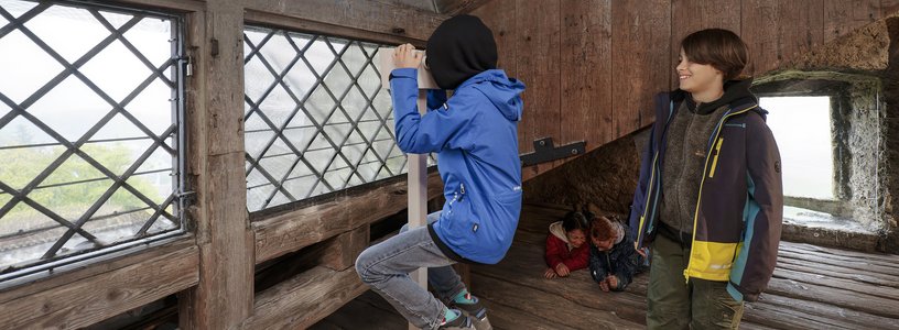 Zwei Schüler unter dem Dach von Schloss Habsburg; ein Bub blickt durch ein Fernrohr ins Weite.