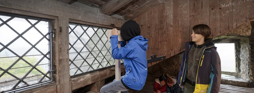 Zwei Schüler unter dem Dach von Schloss Habsburg; ein Bub blickt durch ein Fernrohr ins Weite.