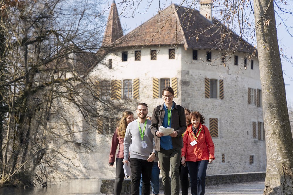 Eine Besuchergruppe mit grünen Foxtrail-Anhängern, im Hintergrund Schloss Hallwyl.