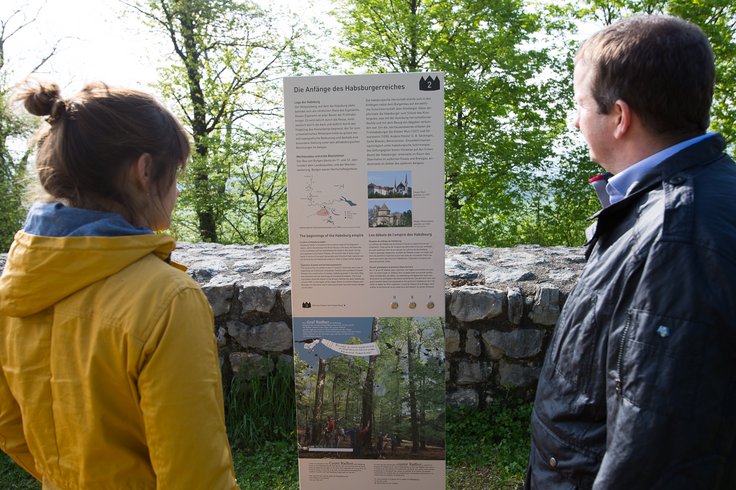 Zwei Besucher*innen lesen die Tafel auf dem Pfad vom Königsweg Schloss Habsburg