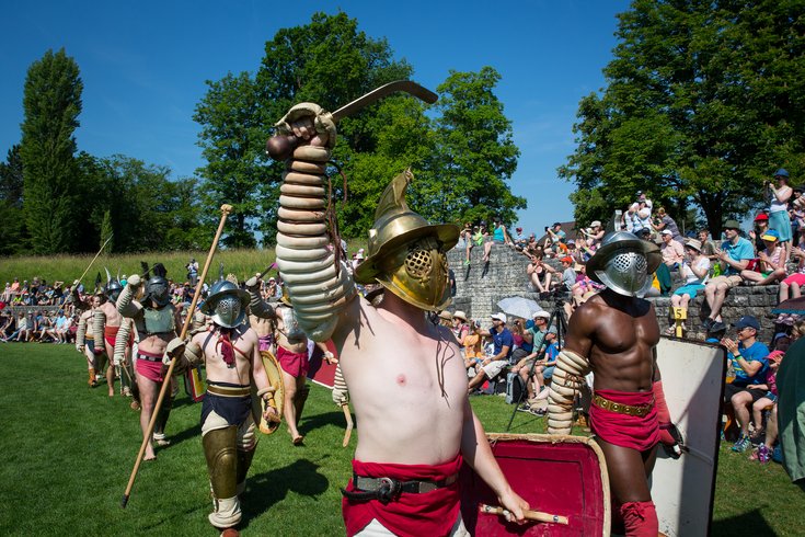 Gladiatoren beim Einmarsch ins Amphitheater Vindonissa. Der vorderste Gladiator hält die Hand triumphierend in die Höhe.