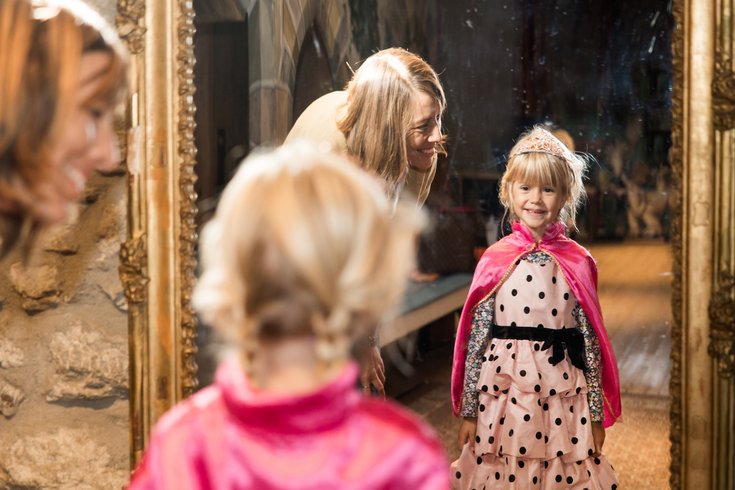 Ein als Prinzessin verkleidetes Mädchen blickt in einen Spiegel im Kindermuseum von Schloss Lenzburg, neben dem Kind steht seine Mutter.