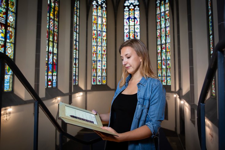 Besucherin schaut auf das Tablet vom Kloster im Hintergrund die farbigen Glasfenstern vom Kloster Königsfelden